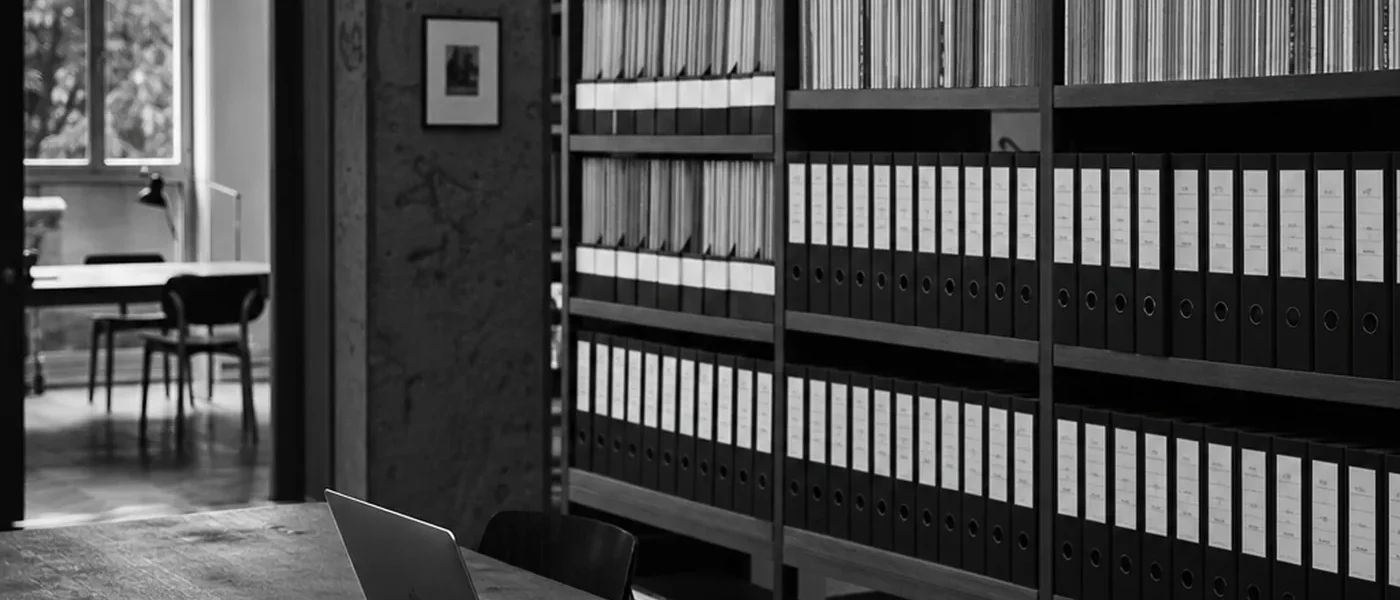 Archivraum mit beschrifteten Ordnern und einem Laptop